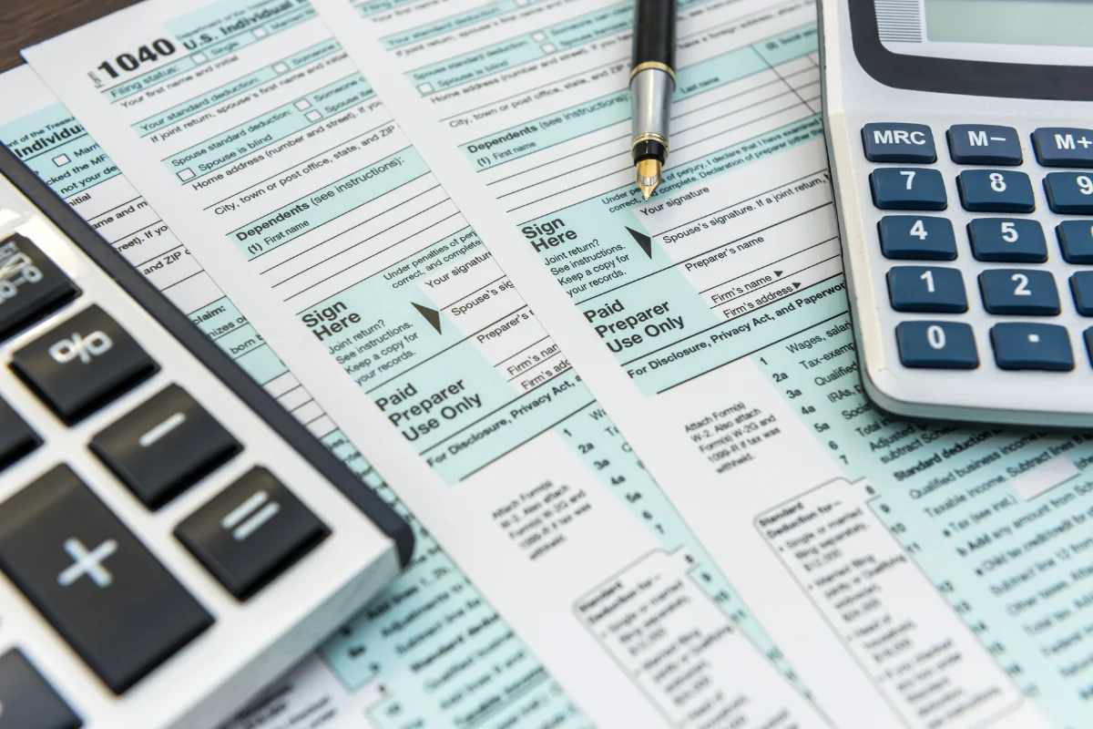 Close-up of tax forms on a desk with a pen and two calculators.